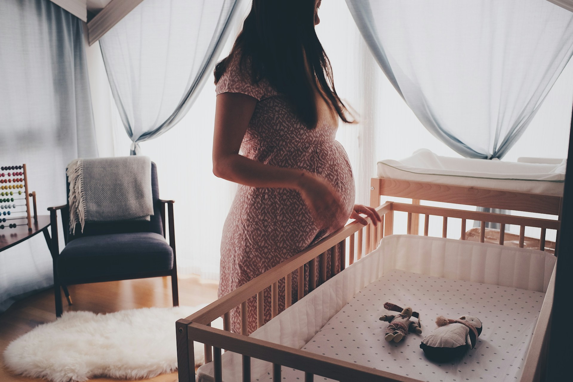 Woman in white lace sleeveless dress standing beside brown wooden crib